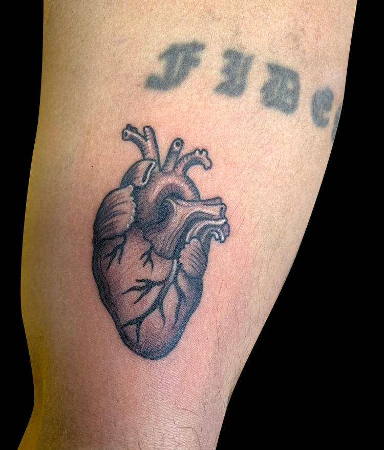 small back and grey tattoo of an anatomical heart just above the elbow
