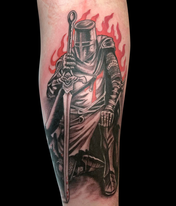 black and grey tattoo of medieval knight kneeling with sword and red flames behind