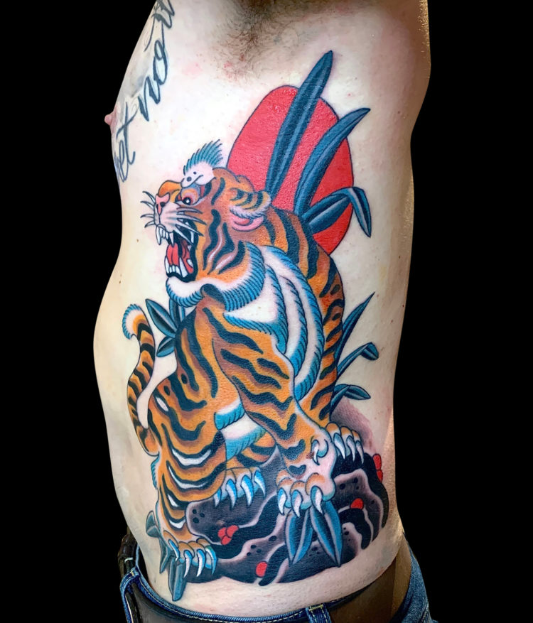 colour tattoo of Japanese dragon climbing on rocks with red sun behind it tattooed on side of body