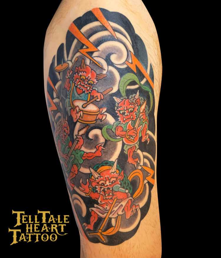colour Japanese tattoo of two onis with musical instruments and black wind bars with orange lightening tattooed on front of thigh