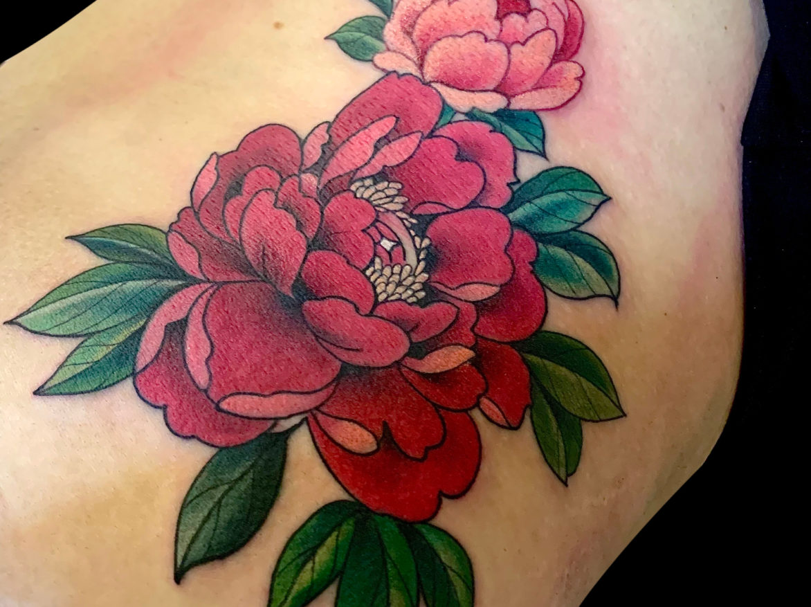 bold colour tattoo of giant pink peonies with green leaves on side of hip and ribs