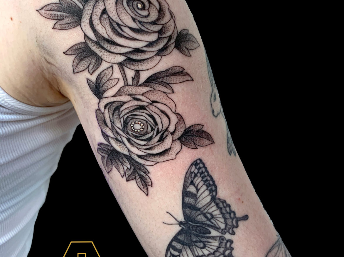 black dotwork tattoo of two stylized roses with leaves on shoulder and arm